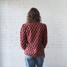 Load image into Gallery viewer, Person wearing a red patterned shirt and blue jeans against a white brick wall.