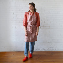 Load image into Gallery viewer, Person wearing a red and white striped apron against a white brick wall.
