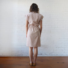 Load image into Gallery viewer, Woman wearing a beige checkered dress standing against a white brick wall.
