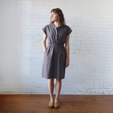 Load image into Gallery viewer, Woman wearing a gray dress standing against a white brick wall.