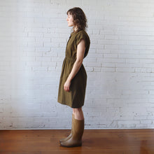 Load image into Gallery viewer, Woman wearing a green dress and boots standing against a white brick wall.