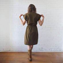 Load image into Gallery viewer, Woman wearing a green dress standing against a white brick wall.