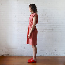 Load image into Gallery viewer, Woman in a pink dress standing against a white brick wall.