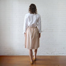 Load image into Gallery viewer, Person wearing a white shirt and beige checkered skirt standing against a white brick wall.
