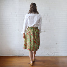 Load image into Gallery viewer, Person wearing a white shirt and green floral skirt against a white brick wall.