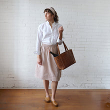 Load image into Gallery viewer, Woman holding a brown tote bag against a white brick wall.