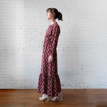 Load image into Gallery viewer, Woman wearing a long floral dress standing against a white brick wall.