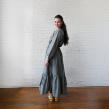 Load image into Gallery viewer, Woman in a checkered dress standing against a white brick wall.