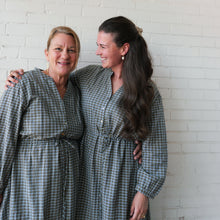 Load image into Gallery viewer, Two women wearing matching plaid dresses standing against a white brick wall.
