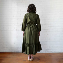 Load image into Gallery viewer, Person wearing an olive green dress standing against a white brick wall.