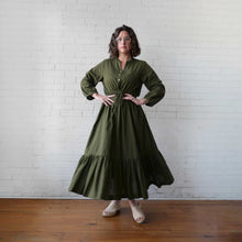 Load image into Gallery viewer, Woman wearing a green dress standing against a white brick wall.