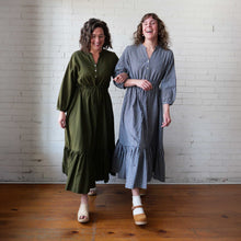Load image into Gallery viewer, Two women standing side by side wearing long dresses against a white brick wall.