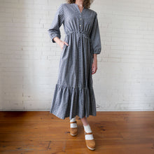 Load image into Gallery viewer, Person wearing a checkered dress standing against a white brick wall.