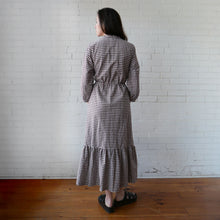 Load image into Gallery viewer, Woman wearing a checkered dress standing against a white brick wall.