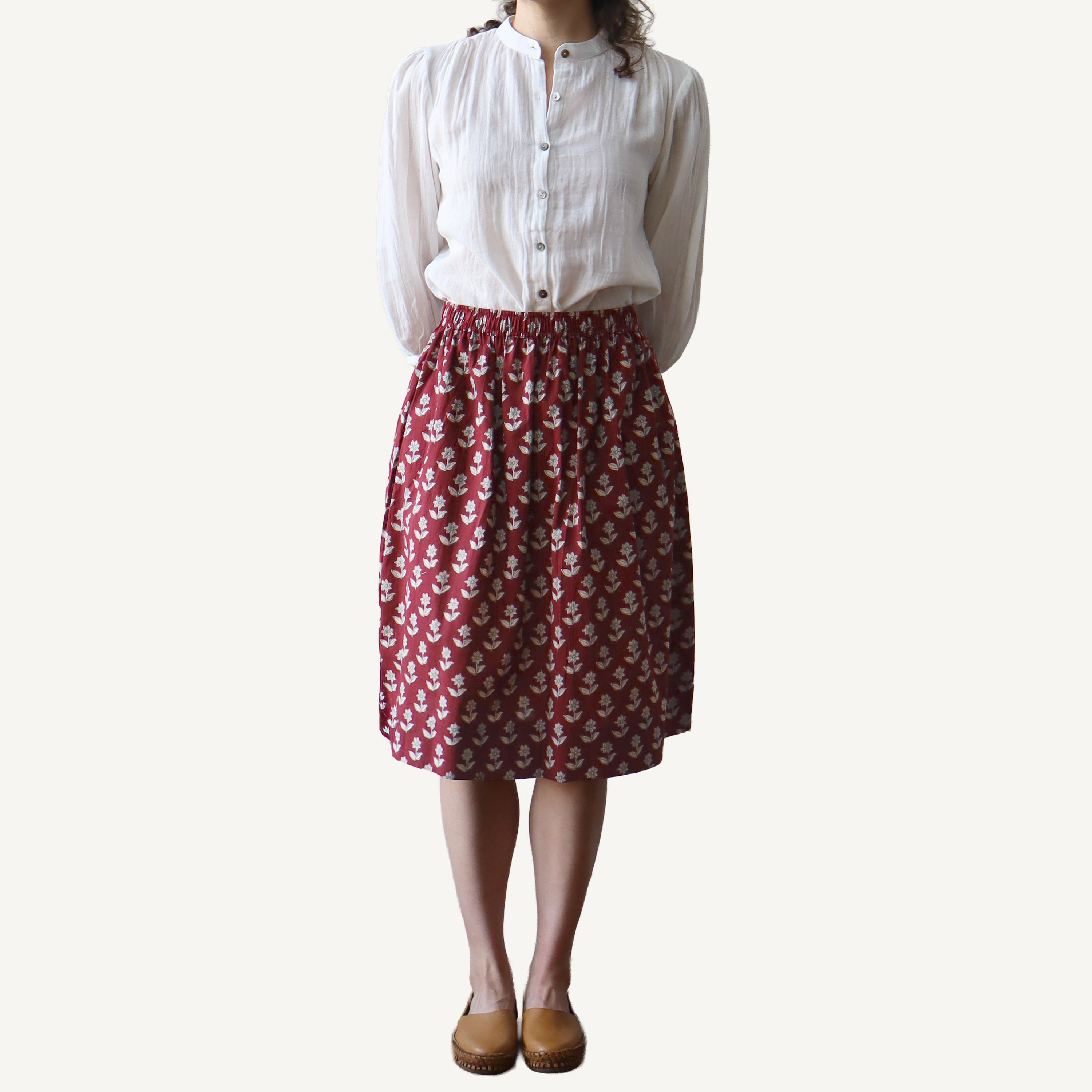 Person wearing a white blouse and red patterned skirt on a plain background