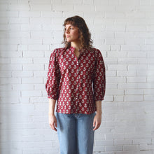 Load image into Gallery viewer, Person wearing a red floral blouse against a white brick wall
