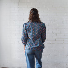 Load image into Gallery viewer, Person wearing a blue patterned blouse and jeans standing against a white brick wall.
