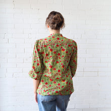 Load image into Gallery viewer, Person wearing a green floral blouse against a white brick wall
