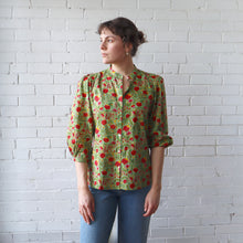 Load image into Gallery viewer, Woman wearing a green floral blouse against a white brick wall

