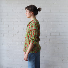 Load image into Gallery viewer, Person wearing a green floral shirt against a white brick wall
