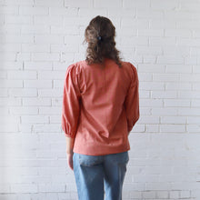 Load image into Gallery viewer, Person wearing a pink blouse and blue jeans standing against a white brick wall.
