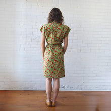 Load image into Gallery viewer, Woman wearing a green floral dress standing against a white brick wall.
