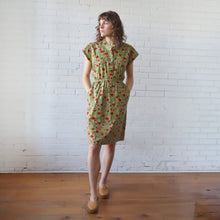 Load image into Gallery viewer, Woman wearing a green floral dress standing against a white brick wall.
