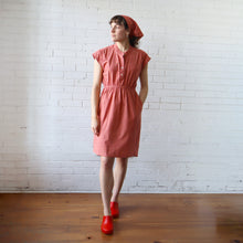 Load image into Gallery viewer, Woman wearing a pink dress and red shoes against a white brick wall.
