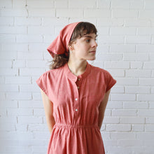 Load image into Gallery viewer, Woman wearing a pink dress and headscarf against a white brick wall
