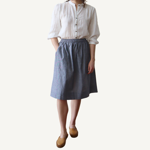 Person wearing a white shirt and blue skirt on a plain background