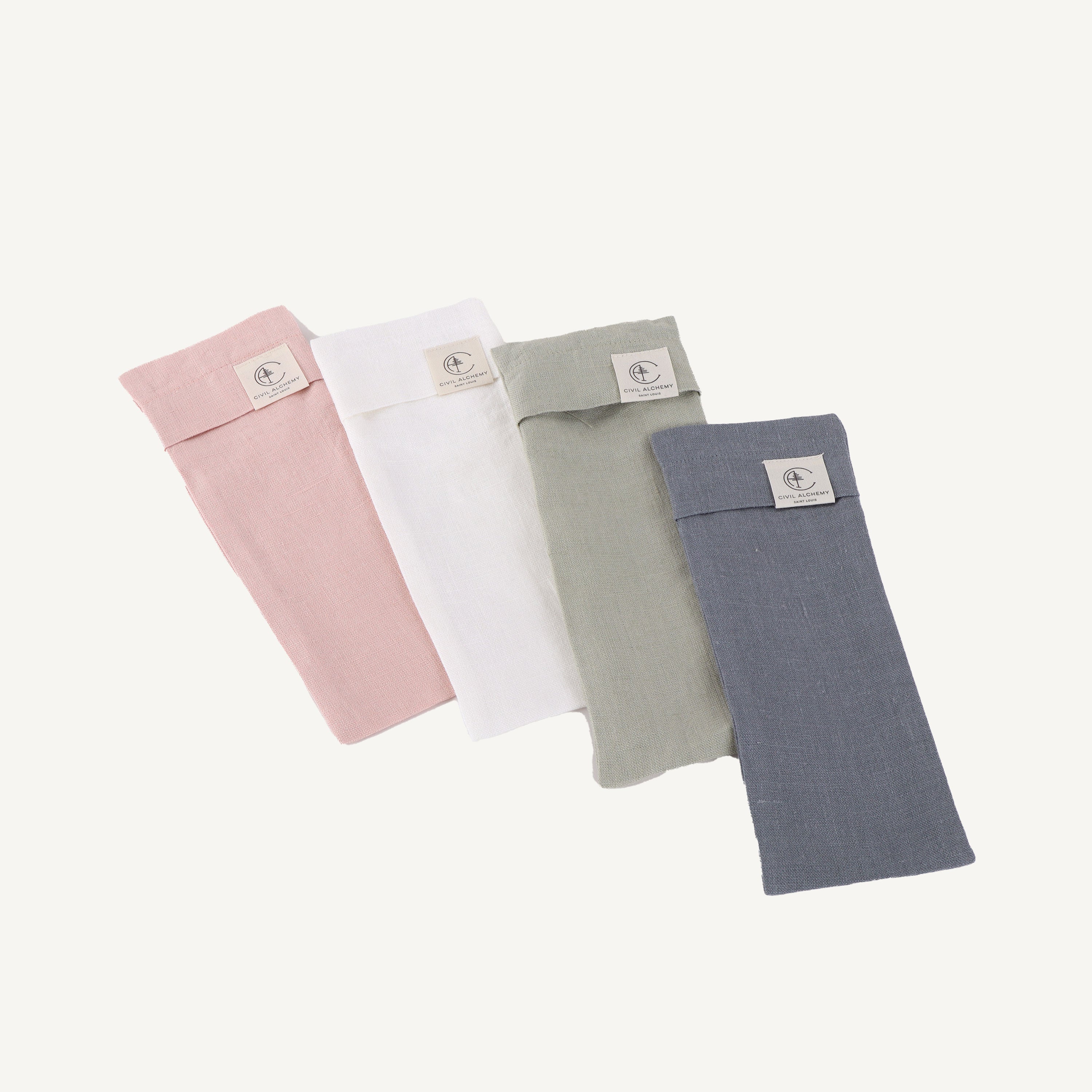 Four folded fabric swaddles in pink, white, green, and blue on a light gray background.