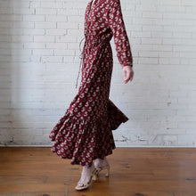 Load image into Gallery viewer, Person wearing a burgundy floral dress against a white brick wall.
