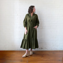Load image into Gallery viewer, Woman wearing a green dress standing against a white brick wall.
