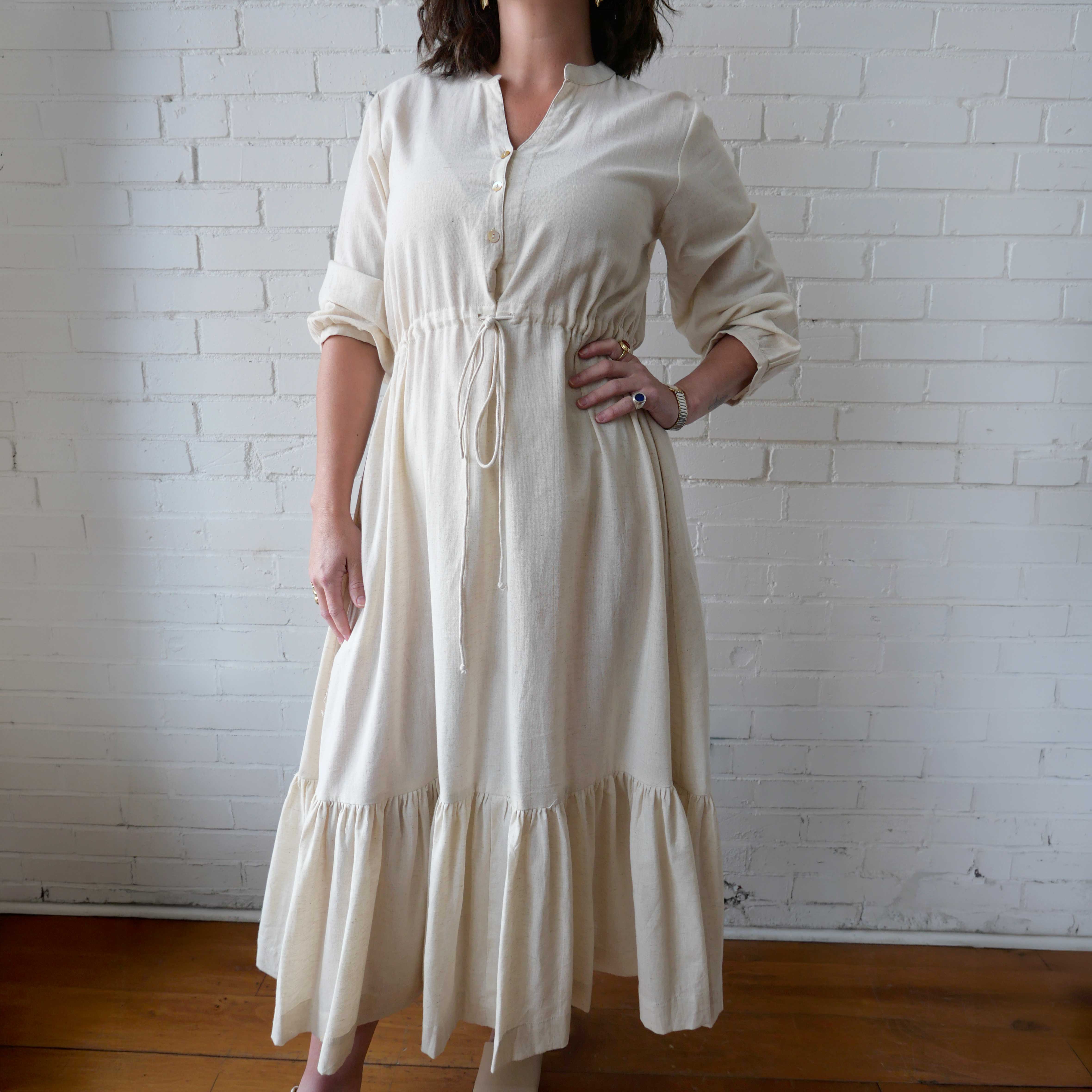 Woman wearing a white dress against a white brick wall.