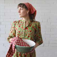 Load image into Gallery viewer, Woman in a floral dress holding a green bowl with a white brick wall background
